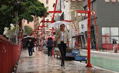 Pedestres se protegem da chuva no bairro da Liberdade durante frente fria na capital.
