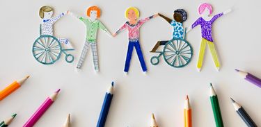 Vários lápis de cor sobre um papel com desenhos de pessoas com ou sem deficiências