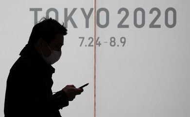 Homem usando máscara de proteção em Tóquio por temor do coronavírus próximo a cartaz de divulgação dos Jogos de Tóquio 2020