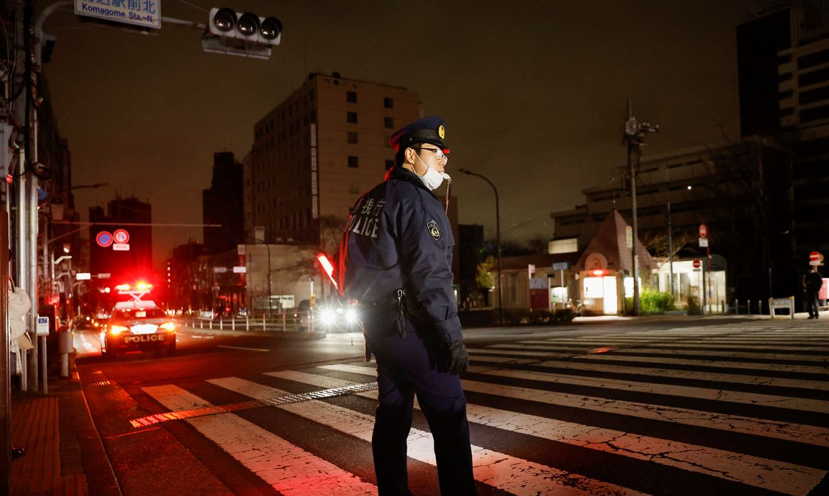 Policial organiza o tráfego de veículos em rua de Tóquio após terremoto cortar energia