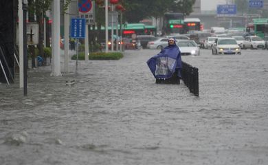 Morador com capa de chuva caminha por rua inundada em Zhengzhou, na província chinesa de Henan.