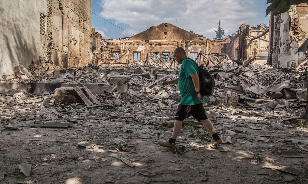 Morador caminha em frente a prédio destruído por ataque militar durante invasão russa na cidade ucraniana de Lysychansk