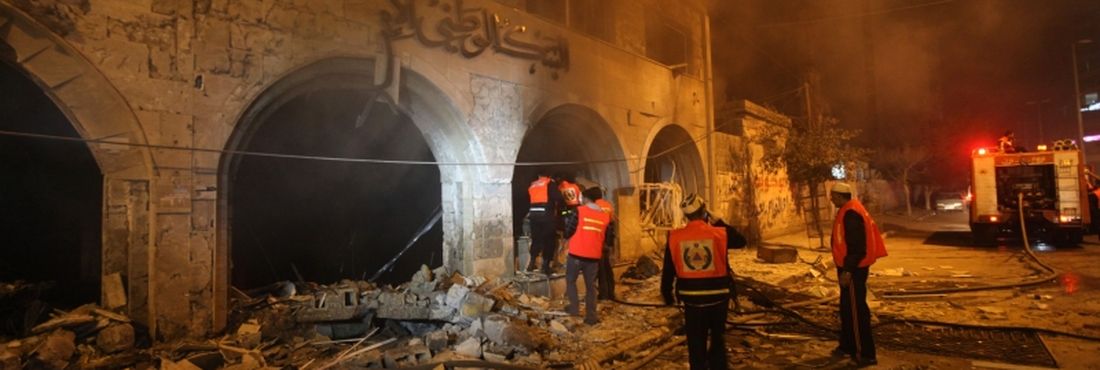 Palestinos tentam apagar um incêndio em uma agência do Banco Nacional Islâmico, após um ataque aéreo de Israel, na cidade de Gaza