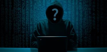 Internet - Crime Virtual: imagem de uma pessoa encapuzada mexendo no computador, o rosto oculto com um ponto de interrogação na frente