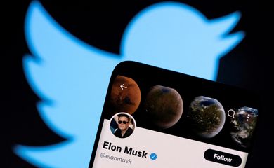 Smartphone mostra a conta de Elon Musk no Twitter em frente a uma projeção do logotipo da plataforma.