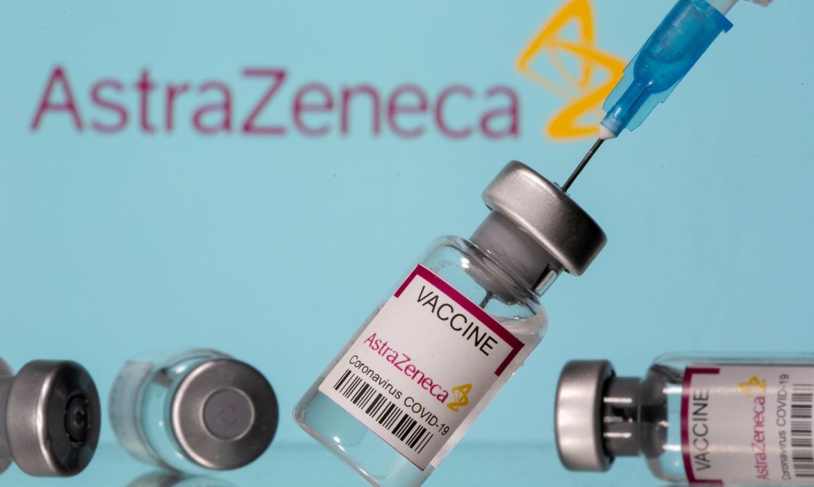Frascos rotulados como de vacina da AstraZeneca contra Covid-19 em frente ao logo da empresa em foto de ilustração