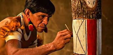Indígena fazendo uma pintura em um tronco