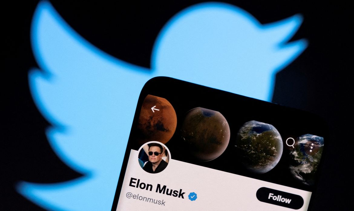 Smartphone mostra a conta de elon musk no twitter em frente uma projeção do logotipo da plataforma.