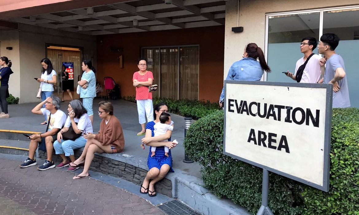 Moradores se sentam do lado de fora depois de serem evacuados do prédio do condomínio após um terremoto na cidade de Makati
