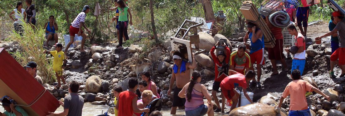 Colombianos deportados da Venezuela carregam seus pertences às margens do rio Táchira