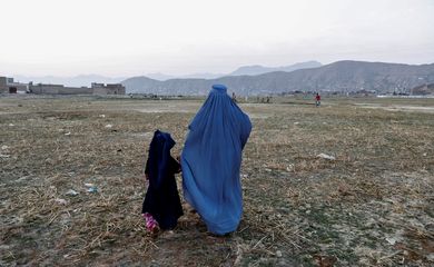 Afegã coberta com burca caminha com menina em rua de Cabul