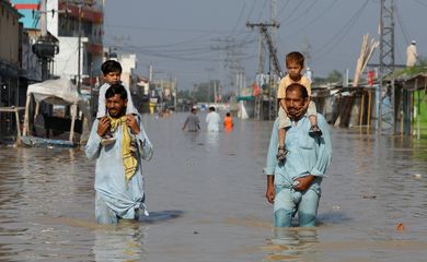 Men carry children on their shoulders and wade along a flooded road, following rains and floods during the monsoon season in Nowshera