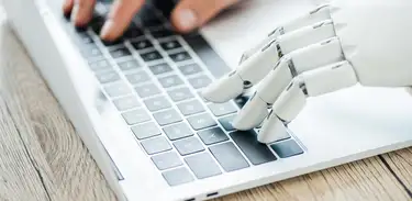 Mão humana e um robô humanoide teclando num computador 