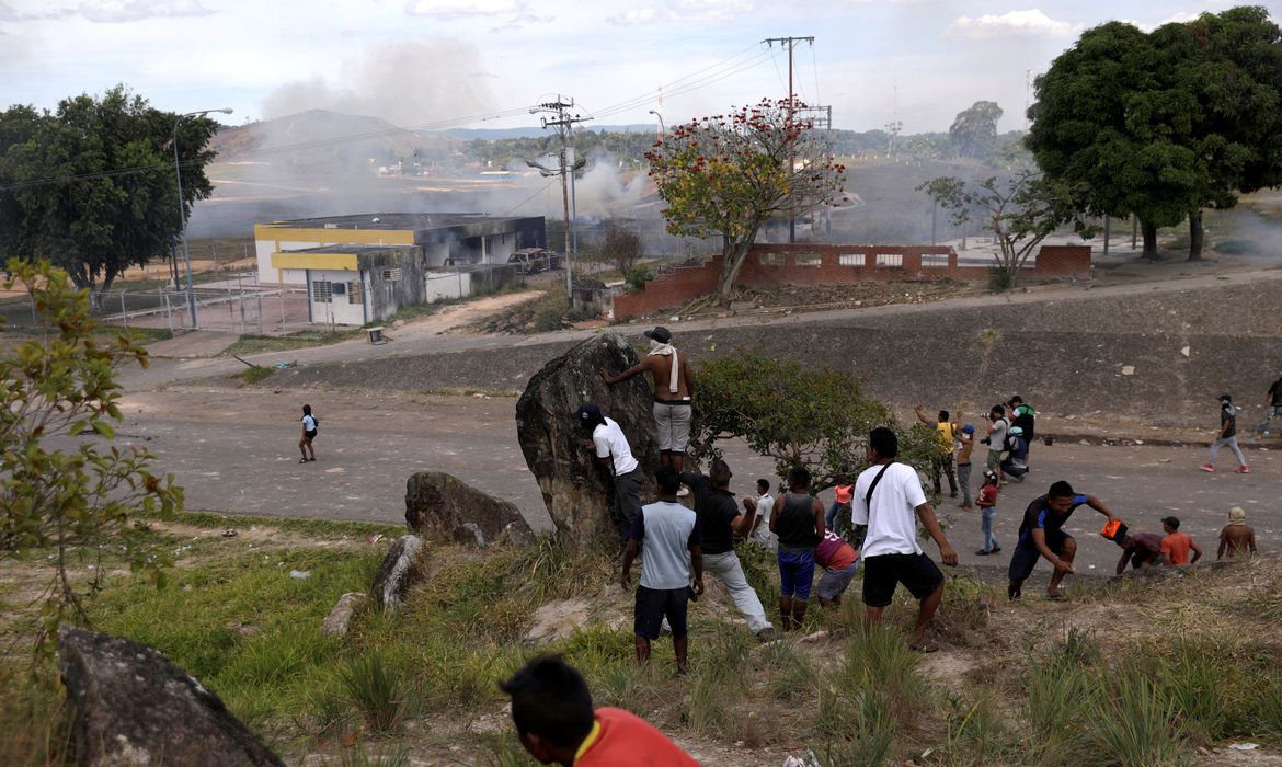 Pessoas se escondem atrás de uma rocha durante confrontos na fronteira venezuelana, em Pacaraima, Brasil 24 de fevereiro de 2019. REUTERS / Ricardo Moraes