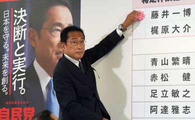 Primeiro-ministro do Japão, Fumio Kishida, coloca papel vermelho ao lado de nomes de candidatos para indicar vitória na eleição para a câmara alta do Parlamento na sede de seu partido em Tóquio