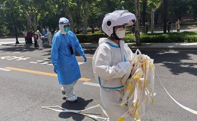 Funcionário em trajes de proteção remove cordão de isolamento de área residencial em Xangai, na China