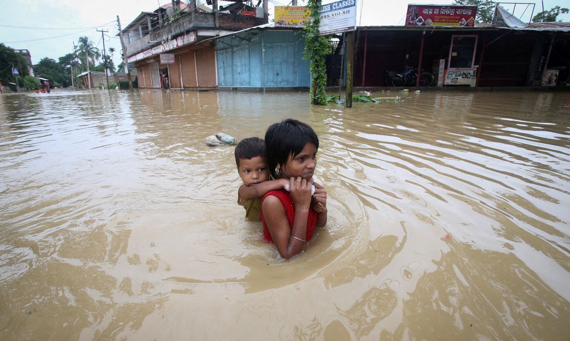 Menina carrega o irmão durante enchentes e chuvas intensas em Bangladesh, na Índia.