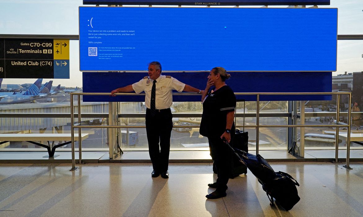 Funcionários da companhia aérea United aguardam à frente de painel de decolagens que mostra uma tela azul de erro, conhecida como 