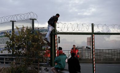 Imigrantes em Calais, na França, escalam uma cerca na tentativa de embarcar em um trem para a Inglaterra