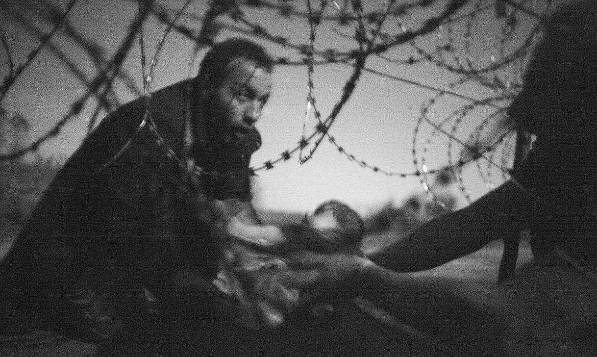 Foto vencedora do World Press Photo de 2016, do fotógrafo Warren Richardson, que mostra o instante em que um refugiado passa seu bebê através de um arame farpado na fronteira húngaro-sérvia, em agosto de 2015