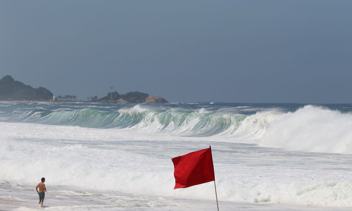 foto de praia com ondas altas e bandeira vermelha em primeiro plano