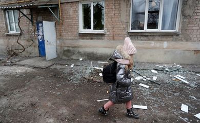 Uma menina passa por um prédio de apartamentos, que moradores disseram ter sido danificado por bombardeios recentes, em Yasynuvata