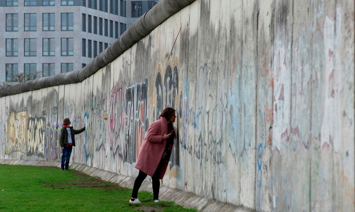 As pessoas tocam os restos do Muro de Berlim no memorial do muro na Bernauer Strasse, em Berlim, Alemanha.