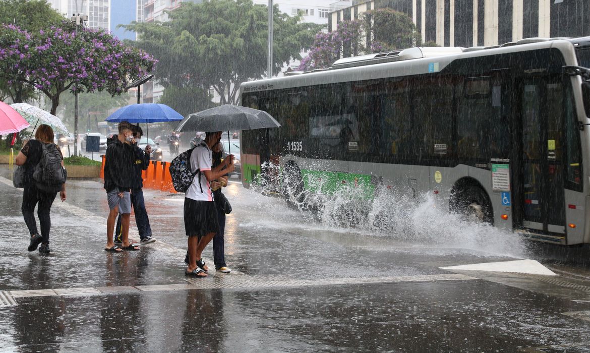 Ônibus joga água na calçada durante chuva na Avenida Paulista.