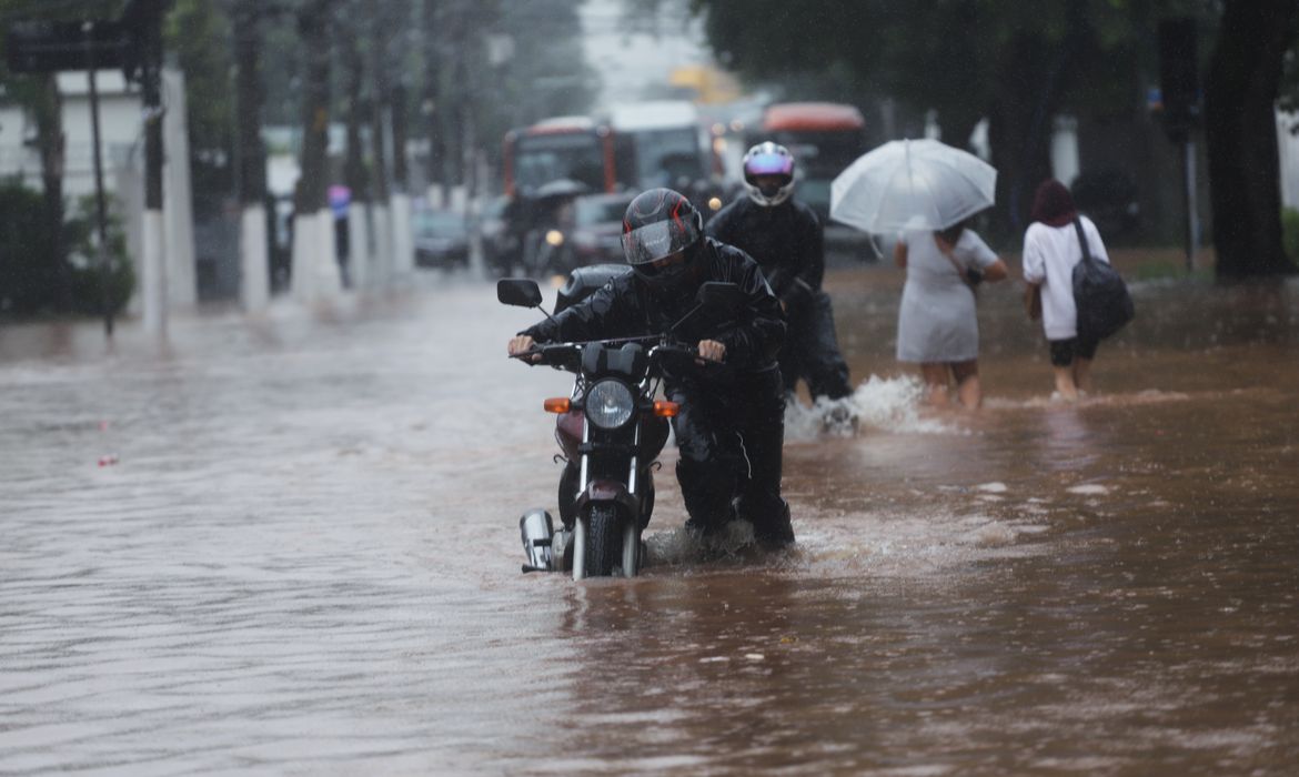 Um homem empurra uma motocicleta por uma rua inundada após fortes chuvas no bairro Butanta, em São Paulo

