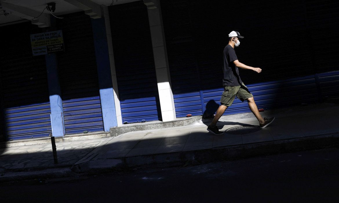 Um homem usando uma máscara protetora passa por um comércio fechado na cidade de Niterói