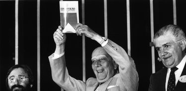 Deputado Ulysses Guimarães sorrindo ao erguer o primeiro exemplar da atual constituição brasileira (1988)