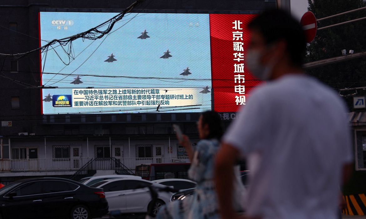 Telão exibe imagens de aviões do Exército de Libertação Popular chinês durante programa jornalístico em cruzamento de Pequim