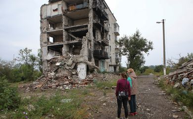 Mulheres olham para prédio residencial destruído por ataque militar na cidade de Izium, na Ucrânia. REUTERS/Vyacheslav Madiyevskyy