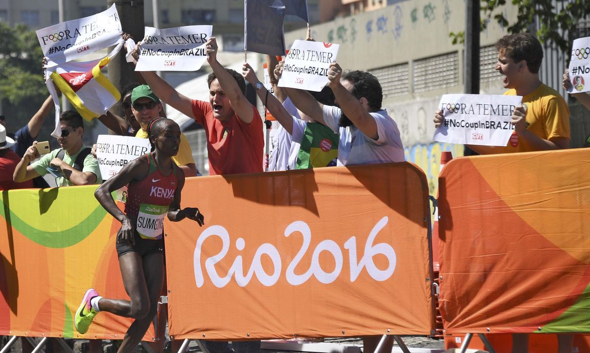 Maratonista passa por manifestantes durante percurso. Na foto, a vencedora da prova, a queniana Jemina Sumgong
