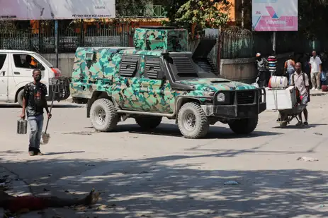 REUTERS/Ralph Tedy Erol SENSITIVE MATERIAL. THIS IMAGE MAY OFFEND OR DISTURB A man walks near a body while a military vehicle patrols after the government declared a state of emergency amid violence, in Port-au-Prince, Haiti, March 4, 2024. REUTERS/Ralph Tedy Erol