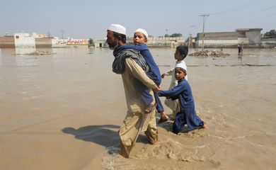 A man walks with children amid flood water along a road, following rains and floods during the monsoon season in Nowshera