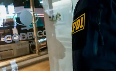 A member of the Investigations Police of Chile stands next to a logo of the Chilean state-run copper producer Codelco, after the company's officials and workers' unions representatives spoke to members of the media about the situation in El Teniente copper mine, where miners have been trapped after a tremor at the Andesita unit, at Codelco's offices in Rancagua, Chile, August 2, 2025. REUTERS/Pablo Sanhueza