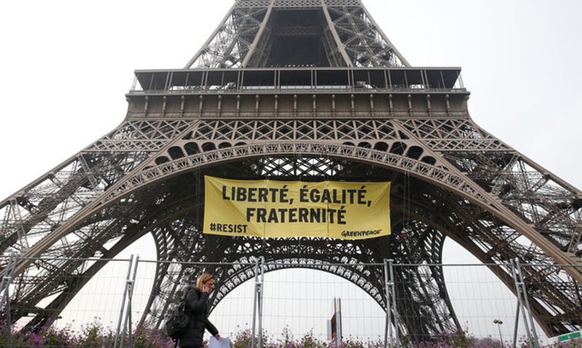 Uma mulher passa pela Torre Eiffel enquanto ativistas do Greenpeace abrem um faixa gigante com 