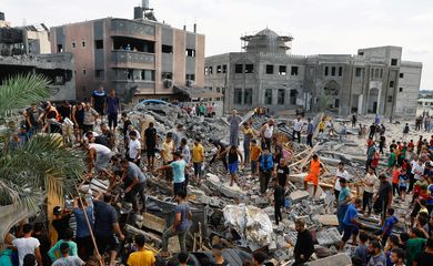 Palestinos caminham em meio a destroços de prédios em Gaza destruídos por ataques de Israel