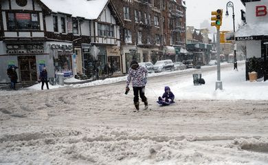 Mulher puxa trenó de criança aproveitando a neve acumulada nas ruas de Nova York