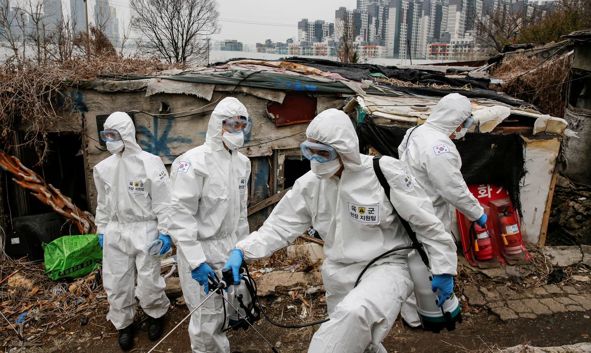 South Korean soldiers in protective gears sanitize shacks as a luxury high-rise apartment complex is seen in the background at Guryong village in Seoul