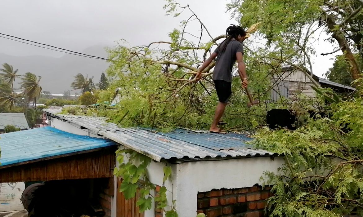 A man removes a fallen branch from the roof of a house, amidst Cyclone Emnati, in Fort Dauphin