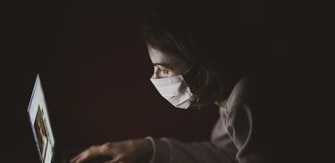 Pessoa de máscara digita em um computador no escuro