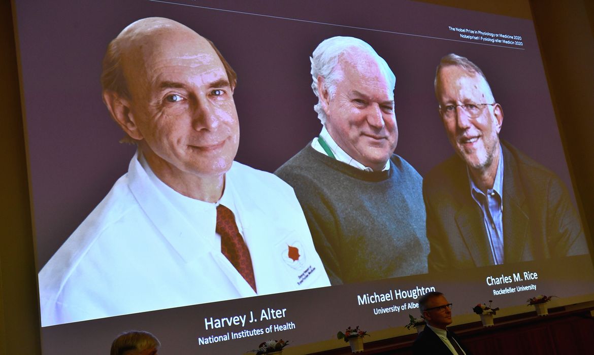 Fotos dos cientistas Harvey J. Alter, Michael Houghton e Charles M. Rice aparecem em tela durante anúncio de vencedores do Prêmio Nobel de Medicina em Estocolmo